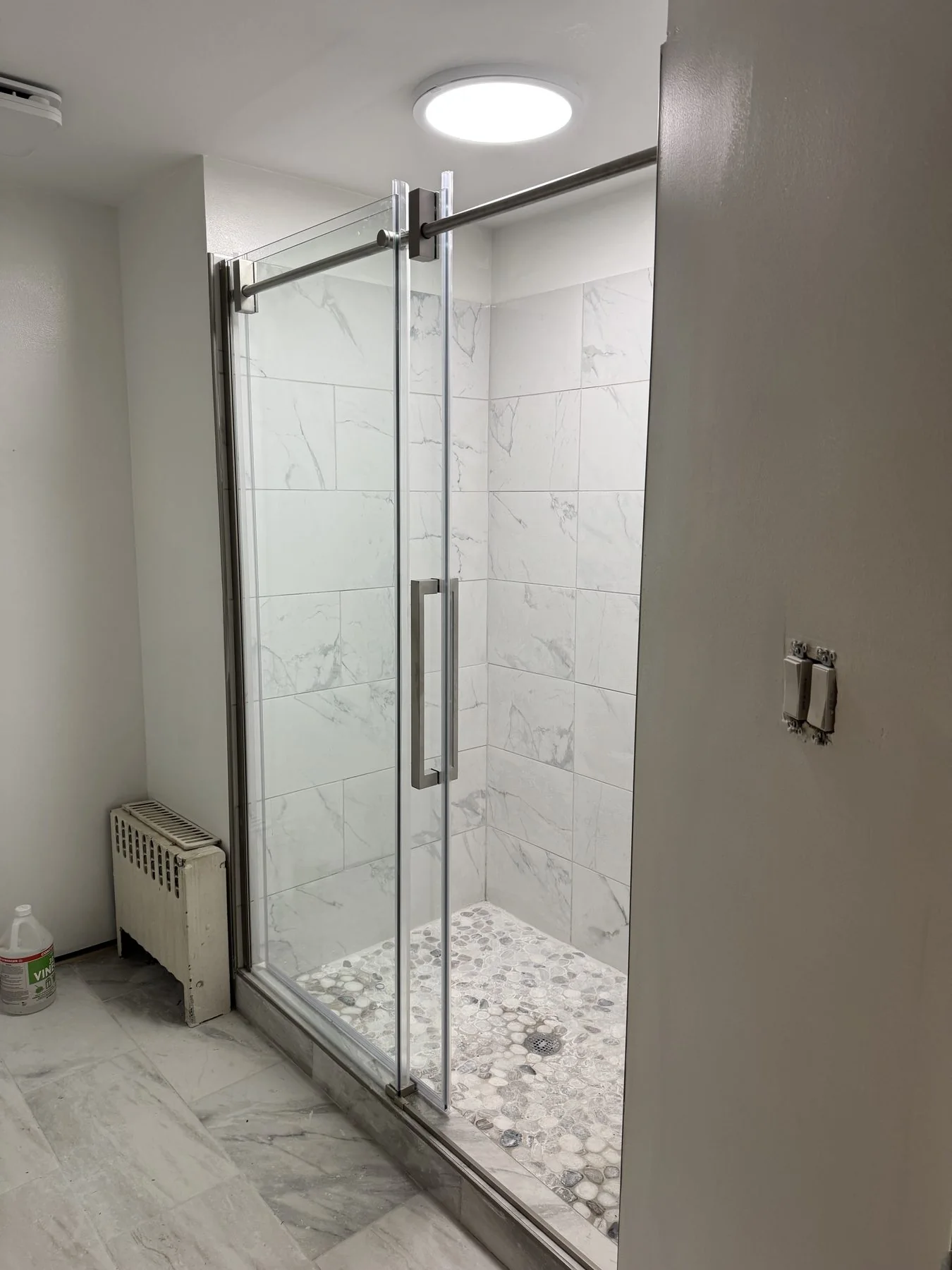 AFTER: frameless glass shower with marble-look tile and pebble floor